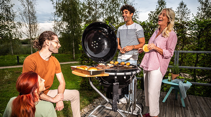 Vier Freunde stehen um den Grill und lachen zusammen.