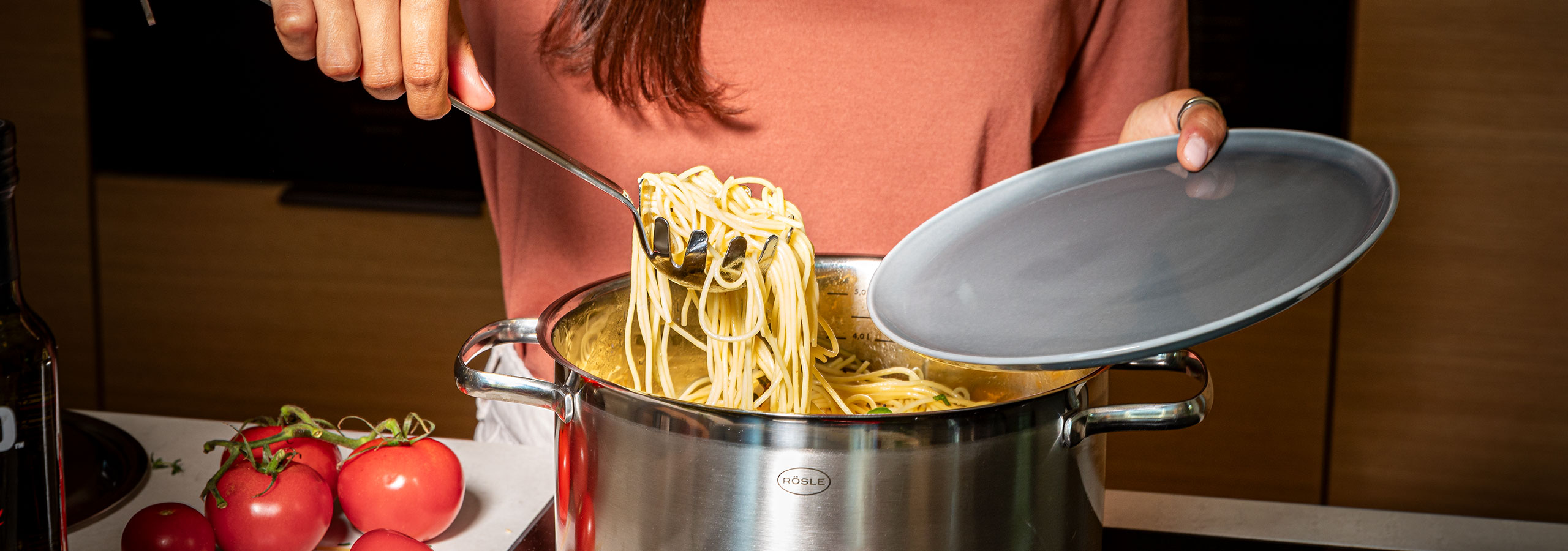 Frau holt mit dem Spaghettiheber Spaghettis aus dem Topf auf einen Teller.