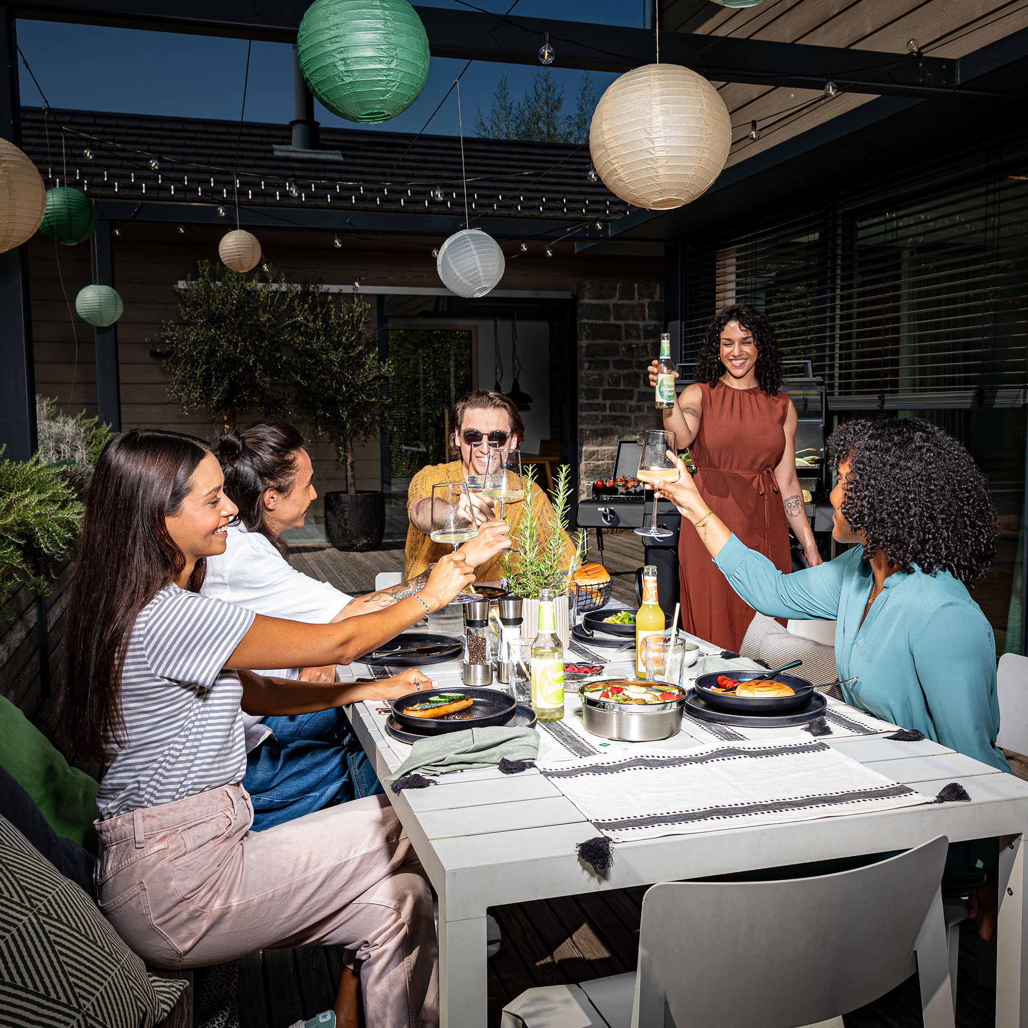 Freunde sitzen zusammen am Tisch auf der Terrasse und stoßen gemeinsam an