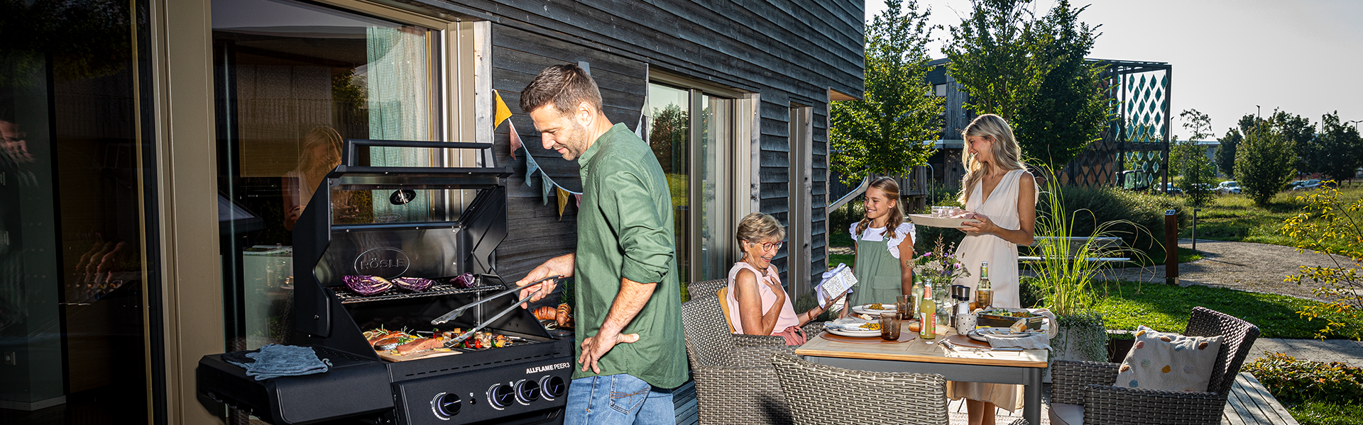 Vater grillt und Kinder und Frau decken den Tisch
